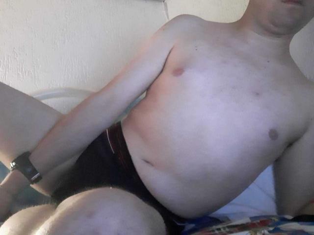 IdrisHot is shirtless, wearing black underwear, with a slightly chubby, pale, and smooth torso, small nipples, and a wristwatch, sitting with legs apart.