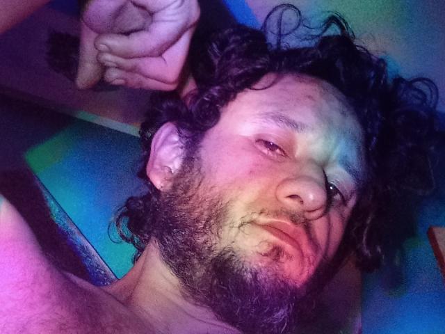 DavydWolfy69 tiene una barba rizada y despeinada, ojos ligeramente rojos y una nariz abultada con un pequeño corte. Su mano está cerca de su cabeza y está sin camisa..