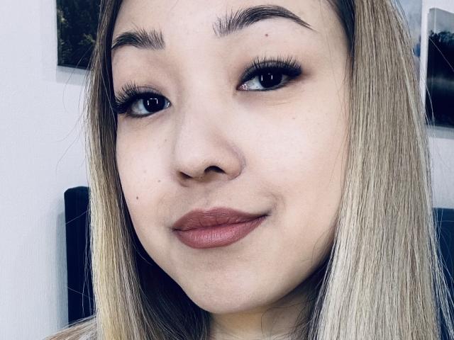 RenyLime's face, showing her blonde hair, full eyebrows, long eyelashes, and pinkish-brown lips. Her skin is light with a few small moles, and she's smiling slightly.