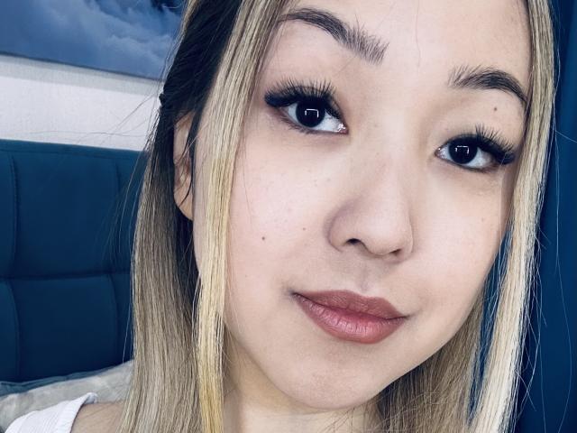 RenyLime has light blonde hair, dark eyebrows, and thick black eyelashes. Her light pink lips are slightly parted. She has a small mole on her left cheek.