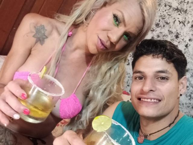 HornyTsBlonde with blonde hair, green eye makeup, pink bra, small tits, holding drink, tattoo on shoulder, smiling. Short-haired guy in green shirt, smiling, holding drink with lime.