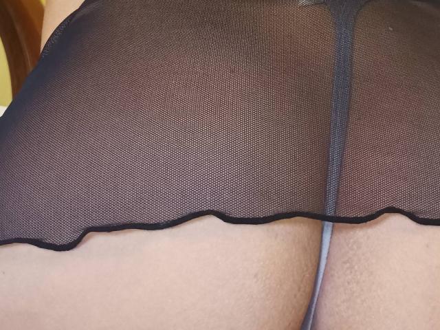 PinkSexyX's ass in a sheer black mesh skirt, showing a black thong and their bare, slightly textured skin. The mesh is wavy at the bottom.
