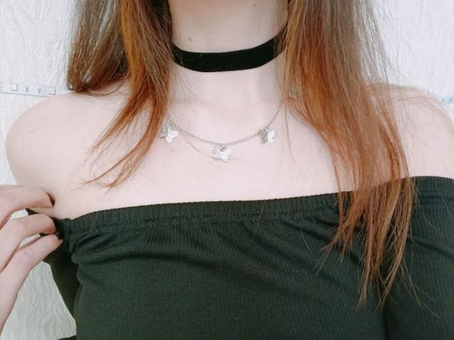 WollyMolly's bare shoulders with a black off-shoulder top, a black choker, and a silver butterfly necklace. Her red hair falls over her chest. Boobs visible.