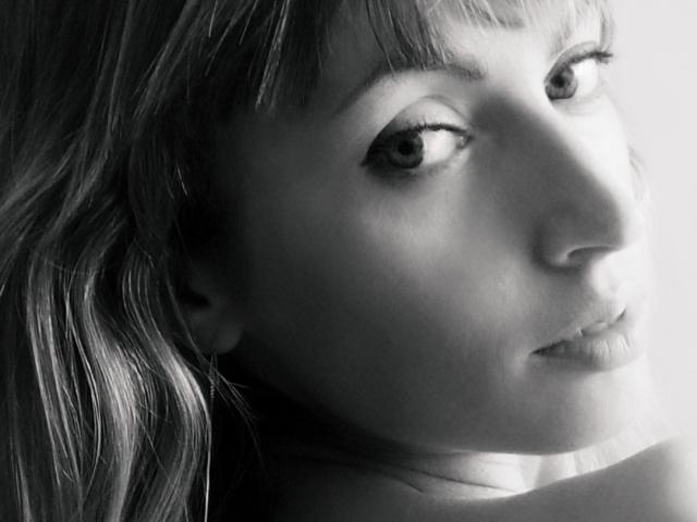 Black-and-white photo of MayaUniverse's face, showing her pouty lips, small nose, and slightly parted eyelids, with wavy hair and subtle eye makeup, looking to the right.