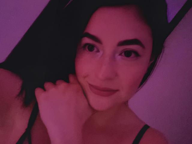 VaaleryStark has dark hair, purple-tinted skin, and a cute smile. She's holding her chin with one hand, wearing a black strap top, and has bunny ears on her head.