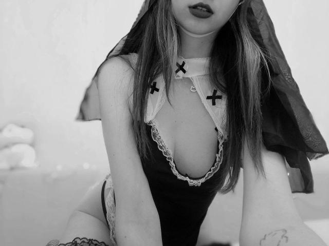 Black-and-white photo of WollyMolly in a sexy maid outfit with lace trim, X-shaped pasties on her tits, and a veil. Her lips are slightly open, showing dark lipstick.
