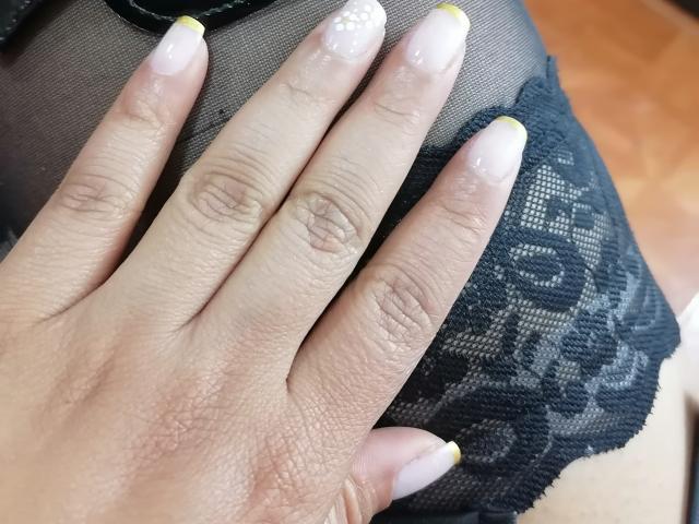 VioletaSwitch's hand with glossy, yellow-tipped nails rests on her black lace bra, showing her slightly tanned skin and textured fingers. Boobs covered by sheer fabric.