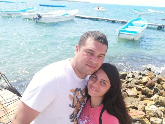 StevenAndPaty, a chubby man with short dark hair, white shirt, and a woman with long dark hair, pink shirt, smiling and leaning on each other by the water.