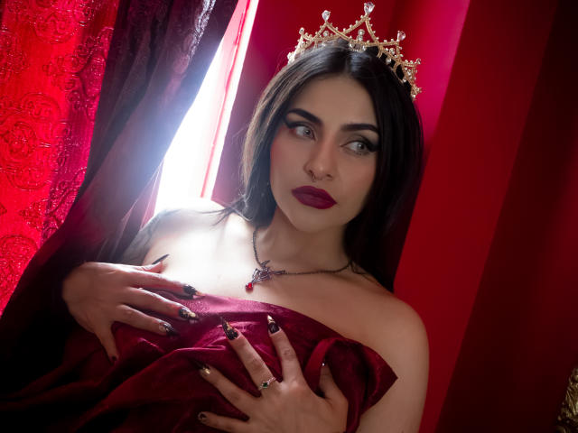 LombanaX with dark hair, red lipstick, black lace dress, large boobs, wearing a gold crown and chain, holding it with her right hand, red jewelry necklace, seductive gaze.