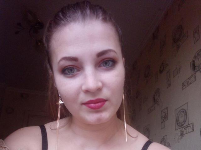 ElizabethHottie has blue eyes, red lipstick, and is wearing long gold earrings. She has light skin, dark brown hair in a bun, and is looking directly at the camera.