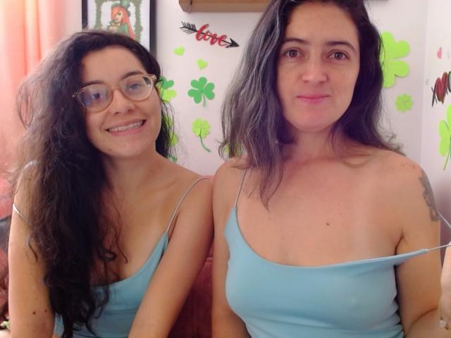 LunaVenus with curly black hair and glasses, and LunaVenus with wavy black hair, both wearing blue tank tops, showing tits, smiling at the camera.