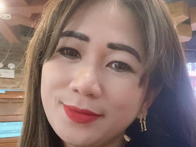 RiverLove's face with brown eyes, thick eyebrows, red lipstick, and long brown hair, smiling softly. She's wearing gold earrings, and her nose is slightly upturned.