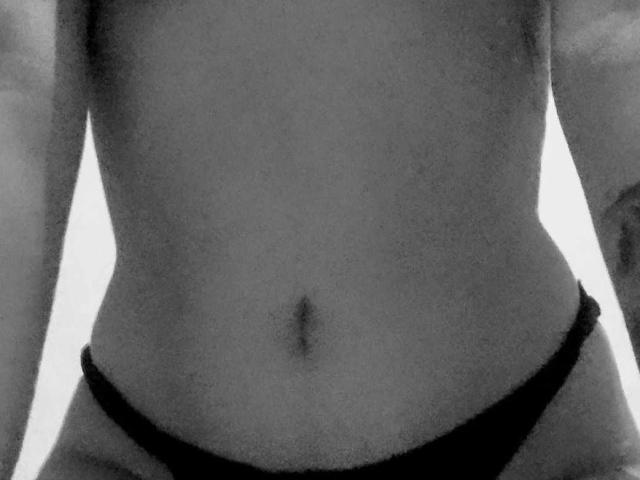 Black-and-white photo of CandyCandyHot's bare midsection, showing a small navel and wearing black panties, with arms slightly visible on the sides.
