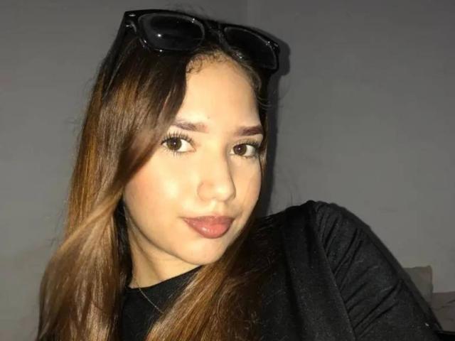 CandyCandyHot has long brown hair, black sunglasses on her head, and is wearing a black shirt. She's looking at the camera with a slight smile.