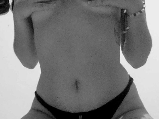 Black-and-white photo of CandyCandyHot, topless, covering her tits with her hands, wearing black panties, showing a flat stomach and a slight belly button.