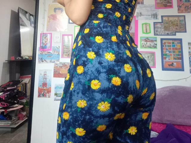 Yukio's ass in a blue dress with yellow daisy patterns, standing with her back to the camera, showing her curvy, tight, and well-defined butt.