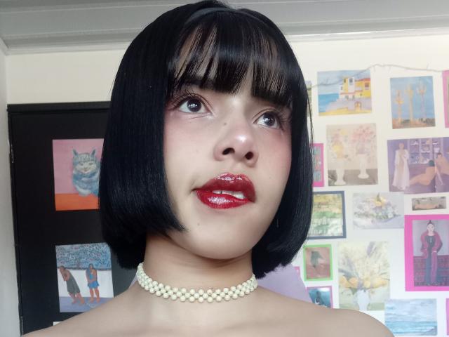 Yukio has shiny black bob, red lipstick, pearl necklace, and brown eyes, staring upward with a slight smile. Boobs not visible, face is the focus.
