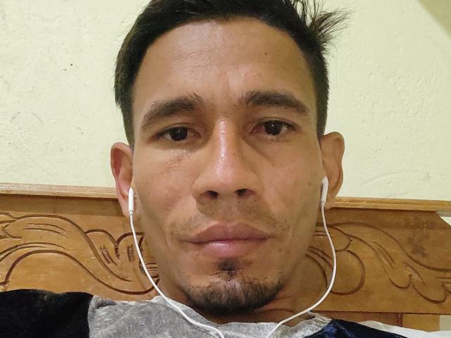 MatiFuego's face, slightly sweaty, with short dark hair, small goatee, and white earbuds in his ears, wearing a dark shirt with a gray patterned collar.