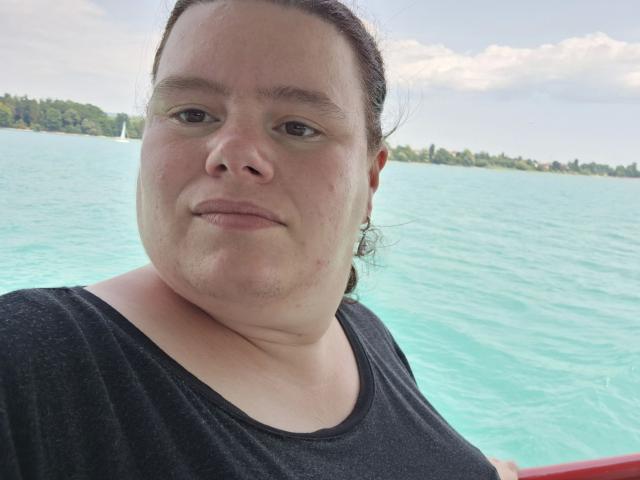 Bbwnicole-hot a un visage rond avec une peau claire, des yeux marron et un léger sourire. Elle porte une chemise noire et ses cheveux sont attachés, et elle est sur un bateau..
