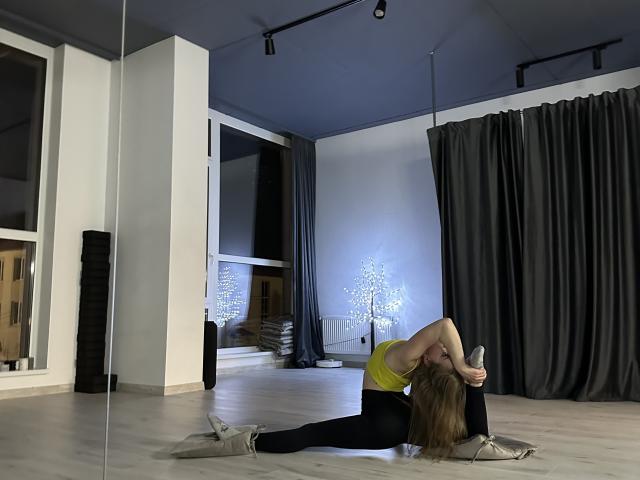 AngellVi, com cabelo loiro, top de ginástica preto e calças legging pretas, segurando um telefone, com uma tatuagem no braço, usando meias brancas, em pé em um quarto iluminado pelo sol, reflexo no espelho..