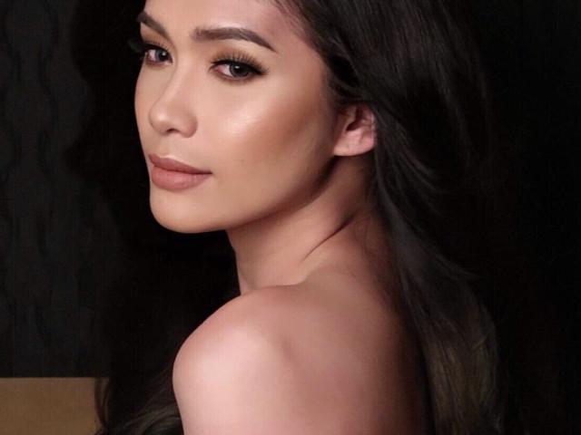 Hikarixmari has smooth, tan skin, long brown hair, and is looking over her shoulder with a subtle smile, showing her bare shoulder and soft makeup.