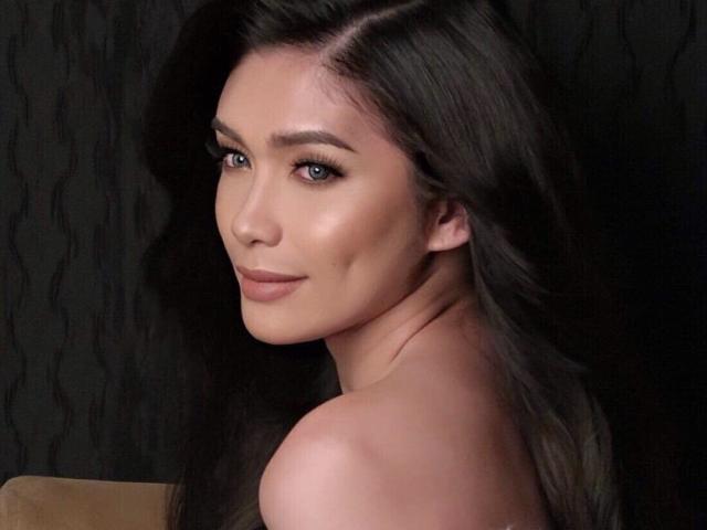 Hikarixmari with long, dark brown hair, light skin, and blue eyes, showing off her bare shoulders and subtle smile, looking over her shoulder. Her tits are partially visible.