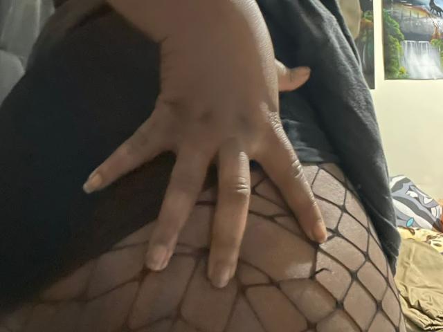 Dilay's hand with fingers spread is resting on her fishnet-covered ass. Her skin is tan, and the fishnets have a diamond pattern. Her nails are short and clean.