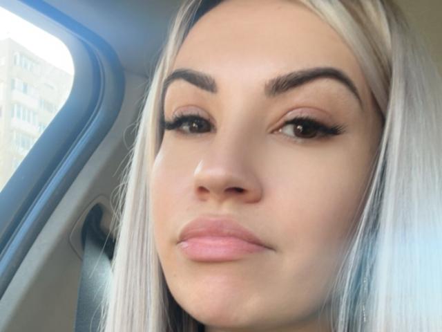 ZoeyMarie's face, with blonde hair, thick eyebrows, long eyelashes, and pink lips, is in a car, looking slightly to the side with a subtle, confident smile.