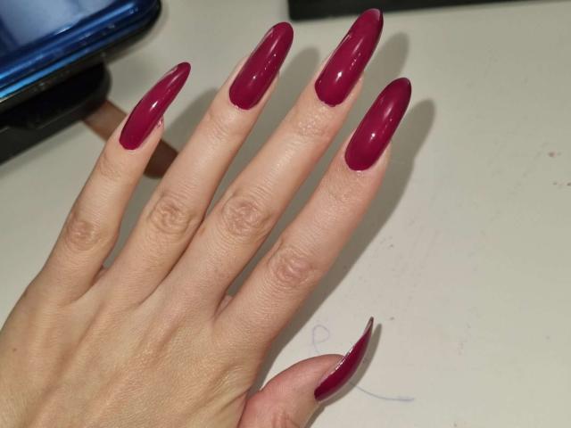 Latrikas Hand mit glänzenden, tiefroten, langen, mandelförmigen Nägeln. Ihre Finger sind gespreizt und zeigen ihre gepflegten, glänzenden Nägel. Ihre Haut ist hell und glatt..
