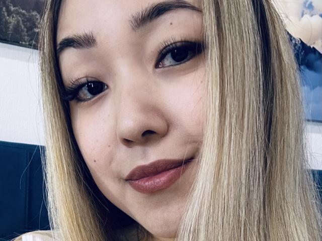 RenyLime's face, showing blonde straight hair, brown eyes, thick eyebrows, long lashes, and pinkish-brown lips in a subtle smile. Her skin is light and smooth.