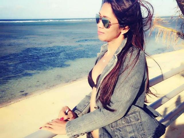 xUrDestinyTS69x-hot with long brown hair, wearing a denim jacket, black bikini, and aviator sunglasses, sitting by the beach, looking off to the side, hands on a white railing.