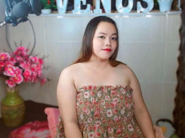BedLover69-hot, chubby, Asian woman with long brown hair, red lipstick, wearing a floral strapless dress, standing, looking at camera, soft smile, medium-sized tits, white tiled wall background.