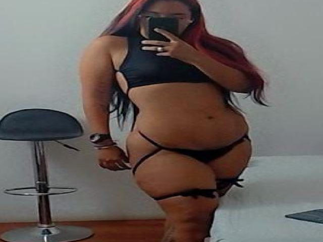 MiaTaylior with long red-black hair, wearing black lingerie, showing her tits, ass, and g-string, taking a mirror selfie, standing by a bar stool.