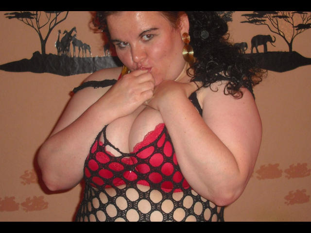 REALAMATEUR - Une femme attrayante avec des cheveux noirs bouclés, une peau bronzée et des boucles d'oreilles dorées, mordant sa doigt tout en suçant son mamelon rose à travers une robe en filet noir et rouge..