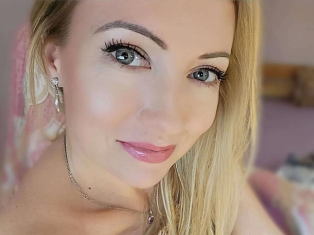 SusiPrivat224-hot ha i capelli biondi, gli occhi verdi e le labbra rosa lucide. Indossa una collana d'argento e orecchini con motivi a croce. Il suo trucco include lunghe ciglia folte..