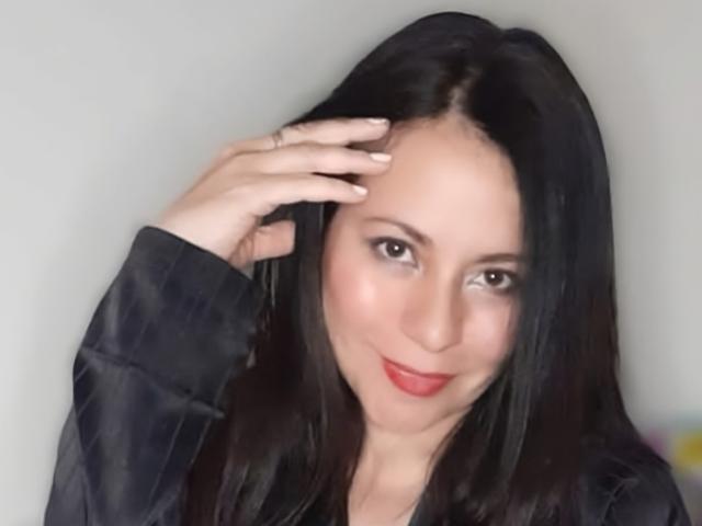 EkaterinaSex with black hair, smiling, red lips, wearing a black shirt, hand in hair, light skin, brown eyes, and a cute face. Boobs not visible.