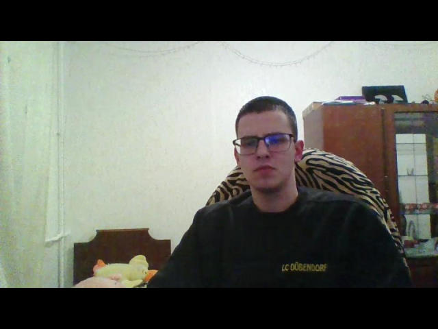 StockingBoy with short brown hair, glasses, and a black shirt, sitting in a zebra-patterned chair, has a slightly puffy ass and a neutral expression.