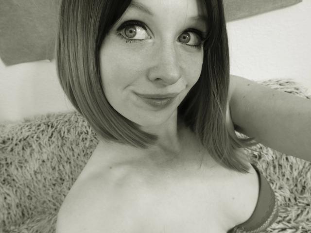 Annekehot-sex with shoulder-length hair, looking up with a slight smile, showing bare shoulders and a hint of a bra, in a grayscale selfie.