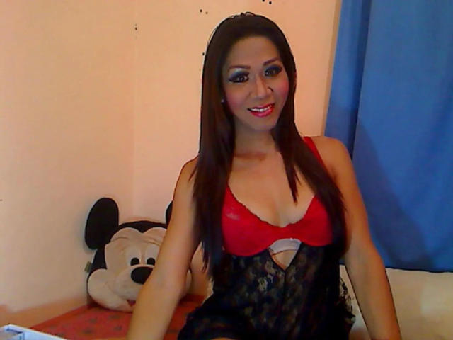 xUrDestinyTS69x-hot with long brown hair, red bra, and black lace lingerie, smiling with red lipstick, sitting on bed with a Mickey Mouse pillow.