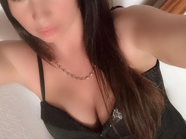 Hot-Strip-Girl with long dark hair, wearing black lace bra, gold chain necklace, showing ample cleavage, slightly blurred face, and raised arm in selfie.