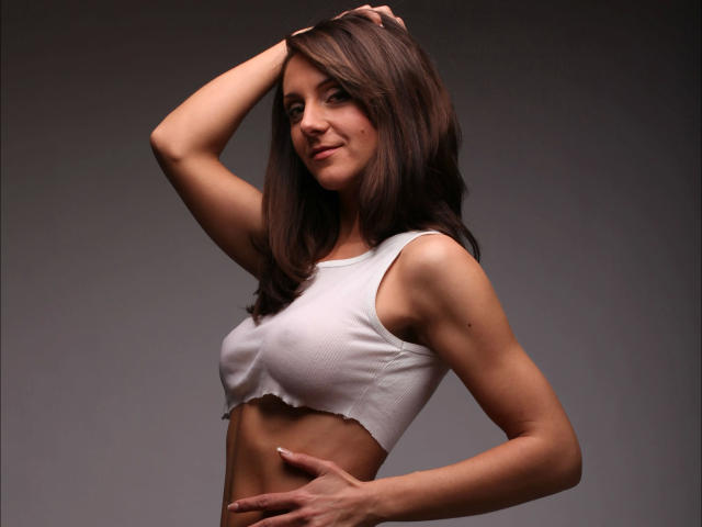 LarisaRais-hot with brown hair, wearing a white crop top, exposing her tits, arm raised, hand on head, midriff visible, slight smile, standing against a dark gradient background.