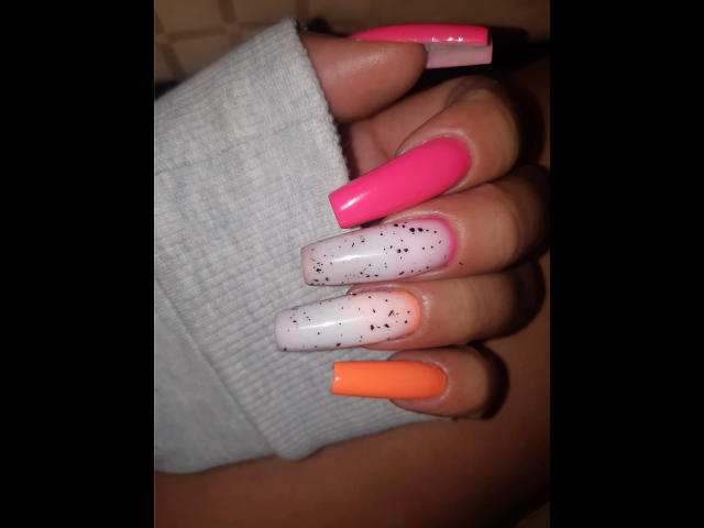 Kostlich-hot's hand with long, shiny nails: pink, pink with speckles, white with speckles, orange. Wearing a gray ribbed sleeve. Nails are super glossy and thick.