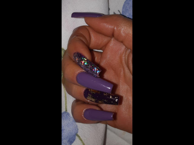 Kostlich-hot's hand with dark skin, long purple nails, glittery nail on middle finger, and rainbow glitter on index finger.
