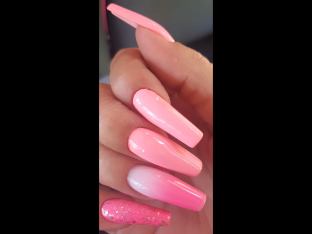 Kostlich-hot's pink ombre nails with long, glossy tips and one nail covered in glitter, showcasing a shiny, smooth finish.