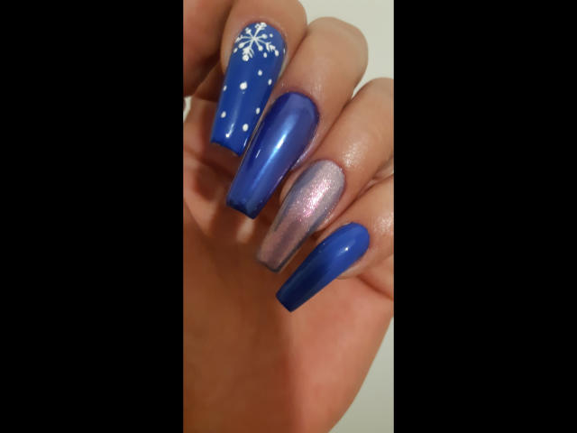 Kostlich-hot's nails are blue with white snowflakes and dots on the ring and index fingers, and a pink glittery middle finger. The other nails are solid blue.
