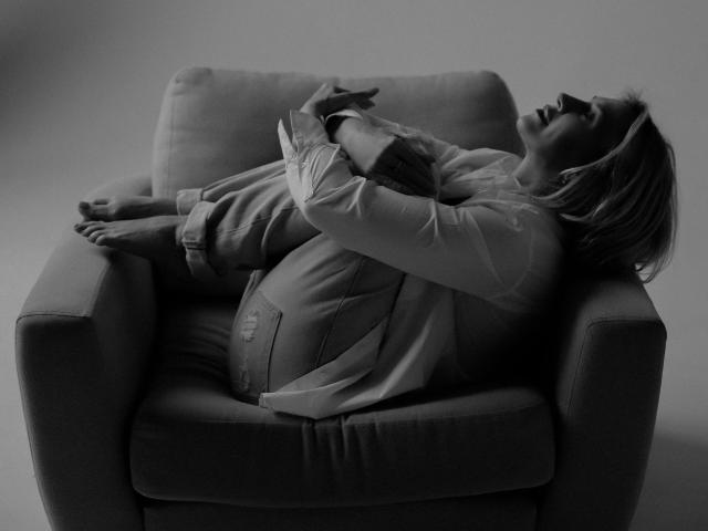 Alessandra93-hot is curled up on a chair, arms hugging knees, head back, eyes closed, wearing a shirt and jeans, bare feet, black and white, relaxed, intimate.