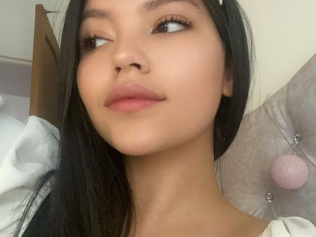 IssaPuasini has long black hair, light brown skin, and full pink lips with a slight smirk. She's looking to the side with a small hair clip in her hair.