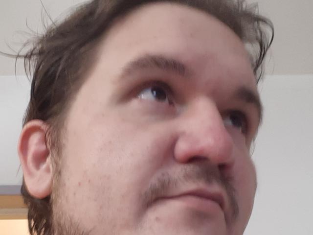 NectarineFad has a slightly dirty face with brown hair, a small mustache, and a subtle smile, looking upwards with a slightly curious expression.