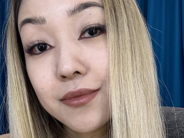 RenyLime has light skin, blonde straight hair, brown eyebrows, dark eyeliner, and pinkish-brown lipstick. Her slightly parted lips give a subtle, confident smile.
