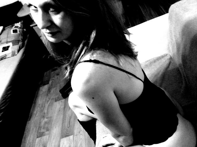Black-and-white photo of SweetElisa1-hot with medium-length dark hair, wearing a black strapless top, showing her bare back and side, with a hand on her butt.